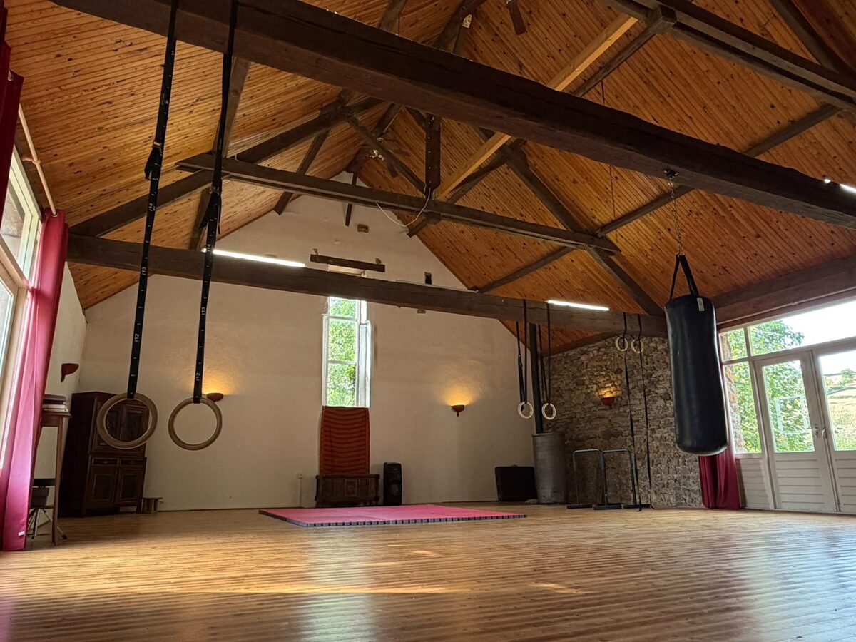 Le studio de pratique de 100 m² : parquet, charpente apparente, anneaux de gymnastique et sac de frappe.
